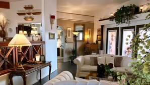 A spacious living room with a sofa, armchair, and a coffee table. There is a lamp on a side table, and a mirror on the wall.