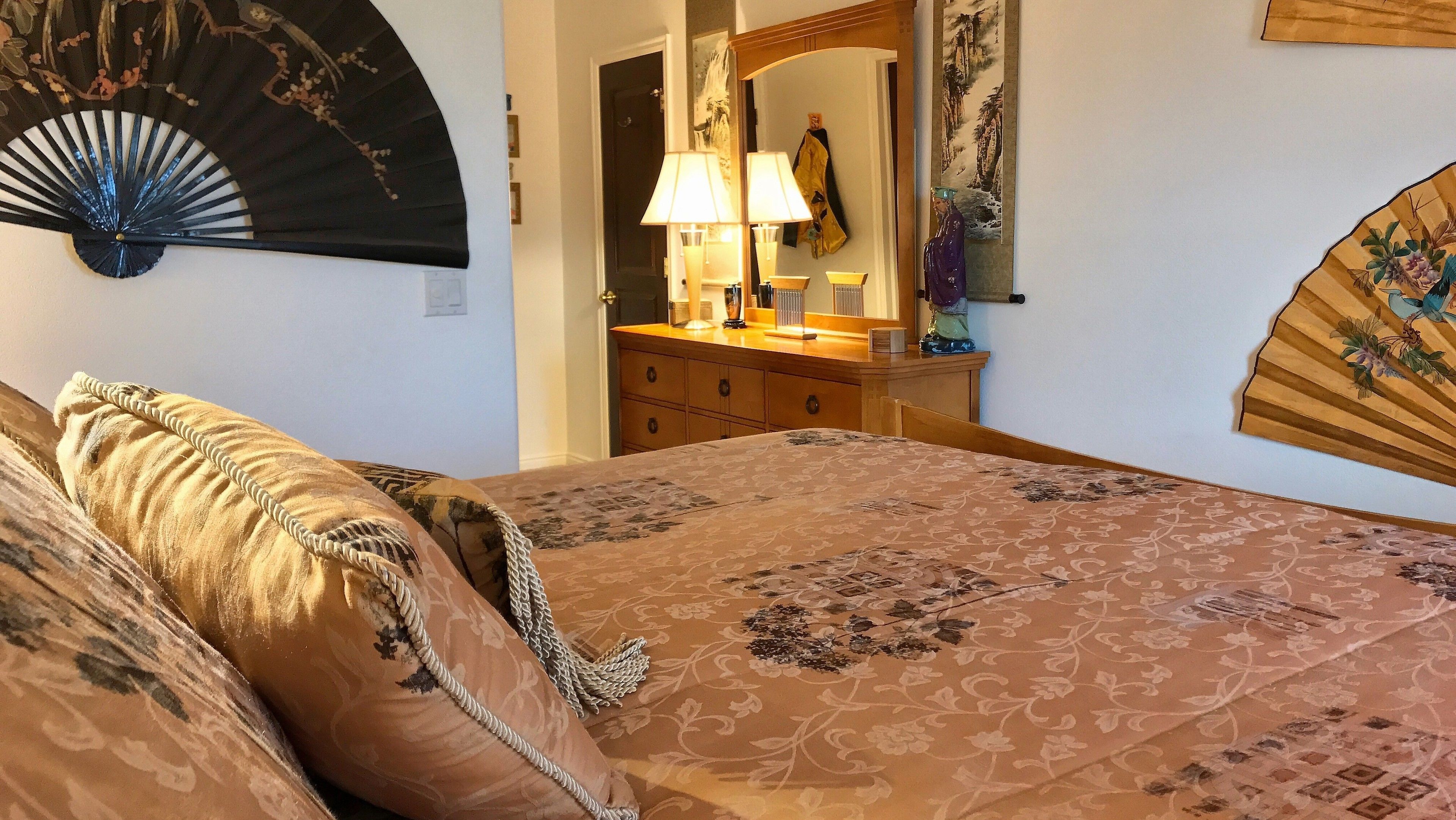 Un dormitorio con cama, cómoda, espejo y ventilador.