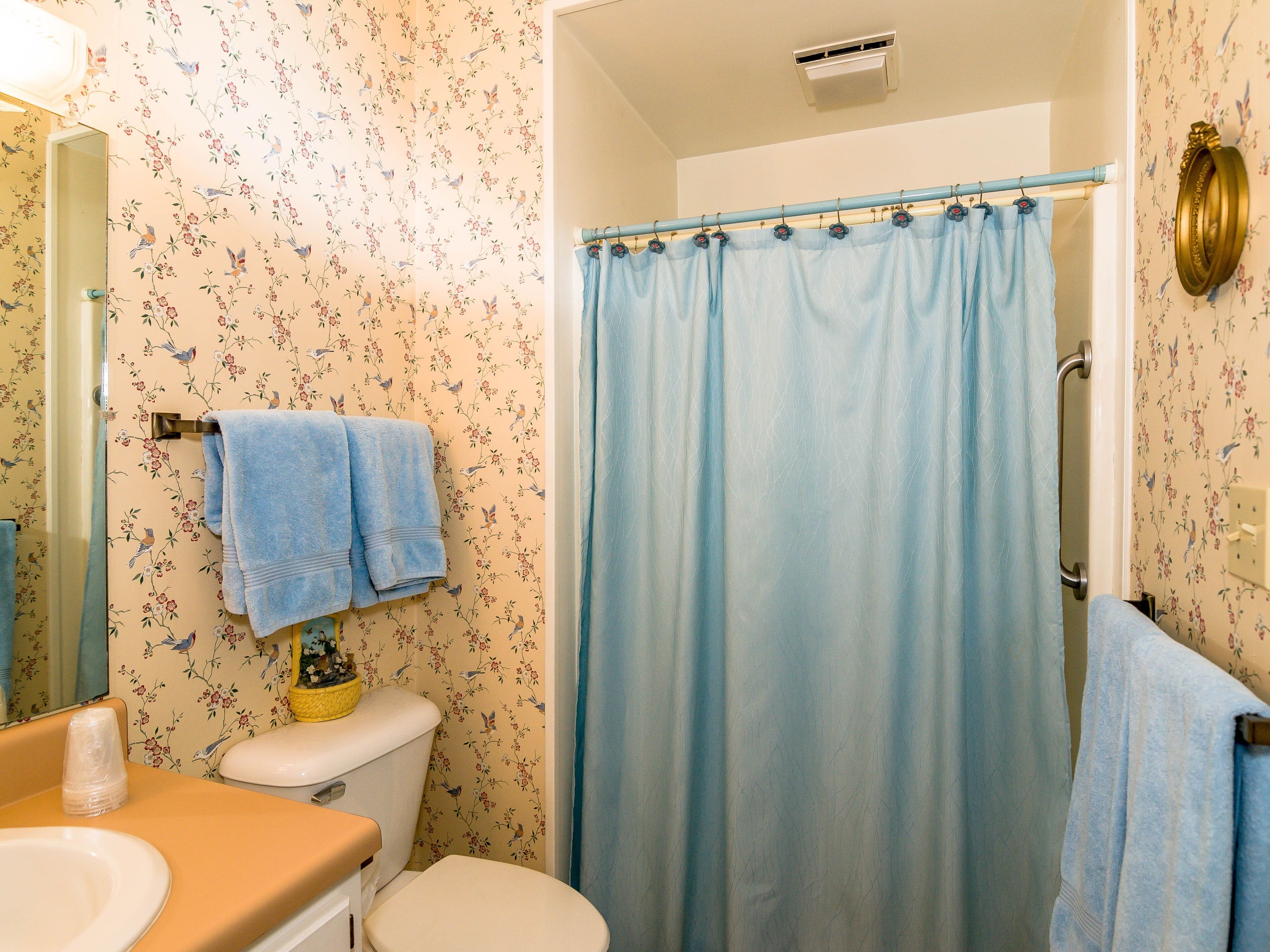 Een badkamer met bloemenbehang, een toilet, een wastafel en een douchegordijn.
