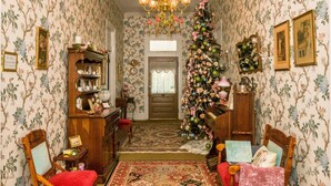 Een gang met bloemenbehang, een kerstboom, een kroonluchter en een piano.