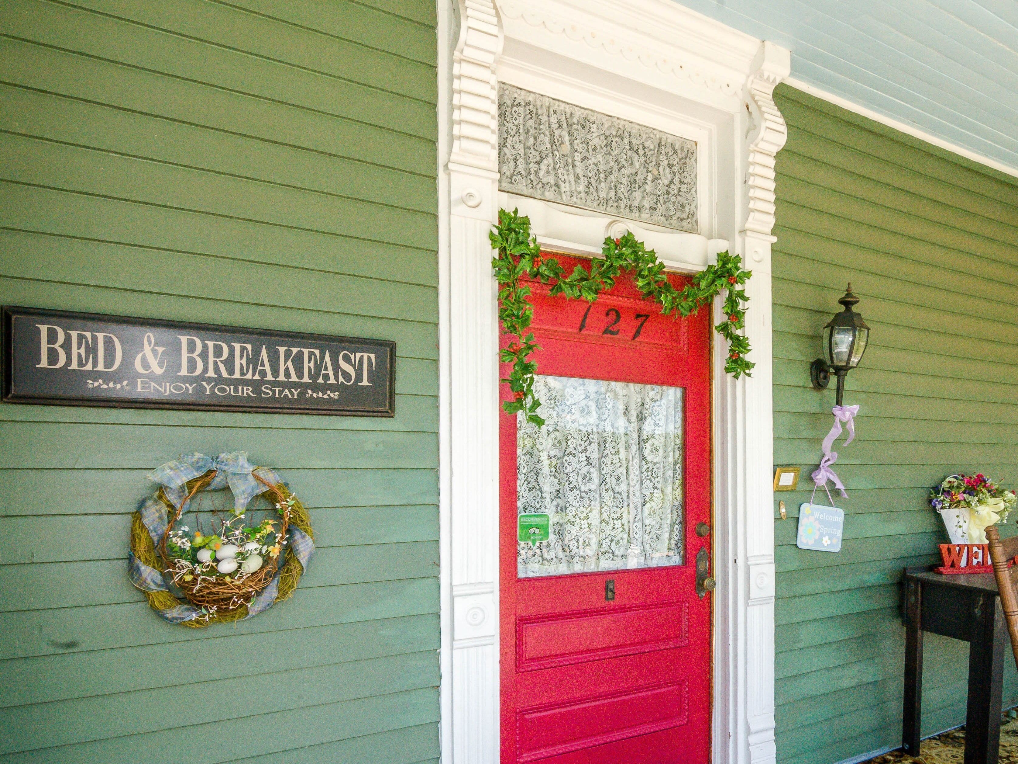 A green building with a red door marked "127" and a sign that reads "BED & BREAKFAST ENJOY YOUR STAY".