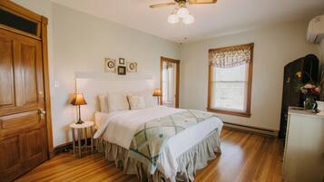A bedroom with a wooden floor, a bed with a quilt, a ceiling fan, and a window with blinds.