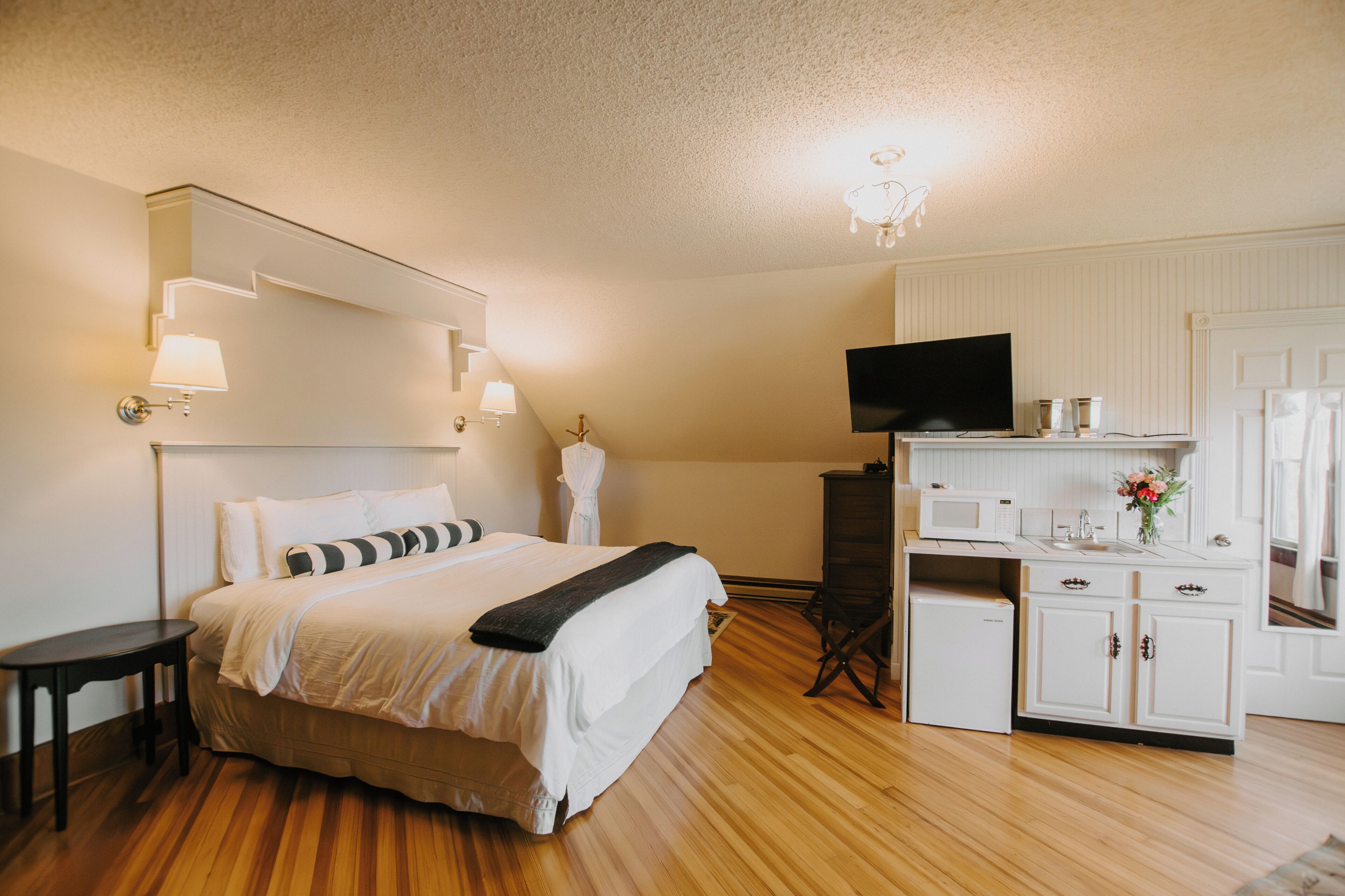 A bedroom with a bed, bedside table, TV, dresser, and a small kitchenette.