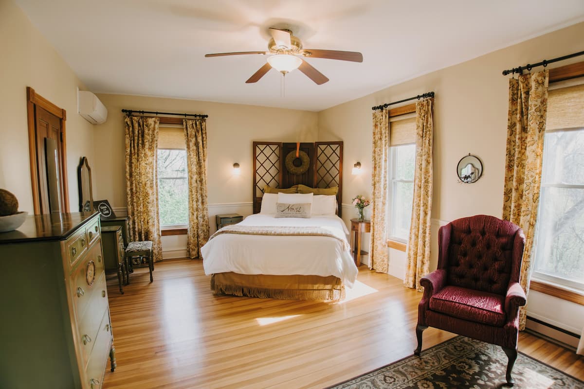 A bedroom with a bed, a chair, a dresser, a ceiling fan, and a window with curtains.