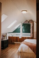 Un dormitorio con tragaluces, un ventanal grande, un banco de madera, una mesita de noche con un florero y una cama grande.