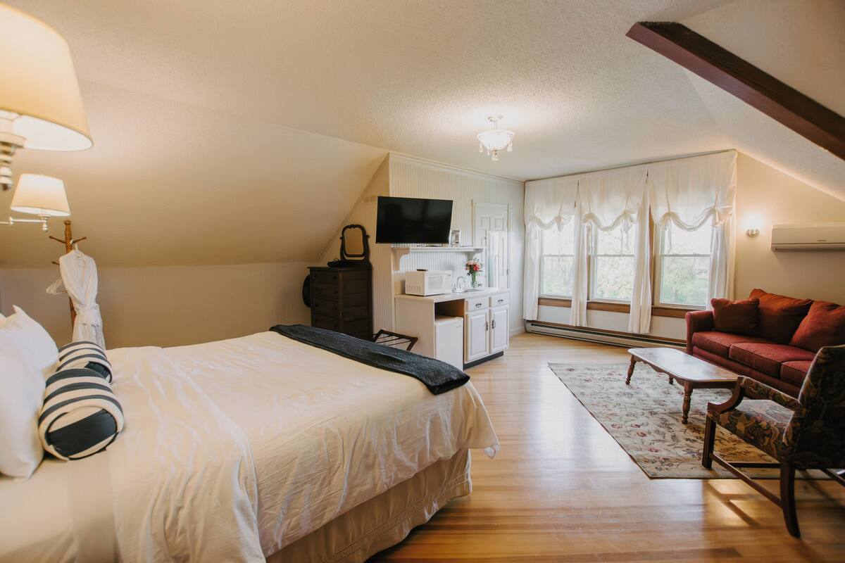 A bedroom with a bed, a television, a dresser, a red sofa, and a window with curtains.