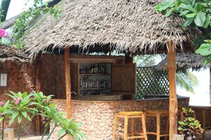 A rustic bar area with a thatched roof, stone walls, and wooden furniture.