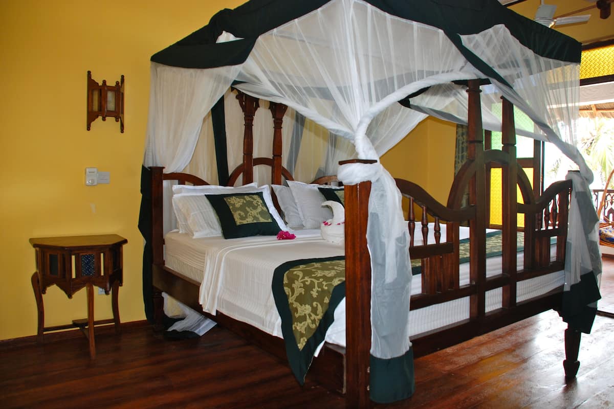 A four-poster bed with a canopy, a wooden nightstand, and a wall-mounted light fixture.