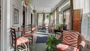 A sunlit room with a dining area, a sofa with patterned cushions, and hanging plants. - Prairie Guest House (Fishers)