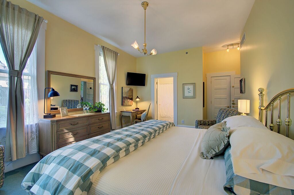 A bedroom with a bed, dresser, bedside table, lamp, and a television on the wall.