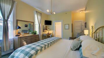 A bedroom with a bed, dresser, bedside table, lamp, and a television on the wall.