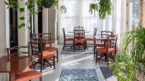 A dining area with a round table, wooden chairs, hanging plants, and a chandelier. - Prairie Guest House (Fishers)