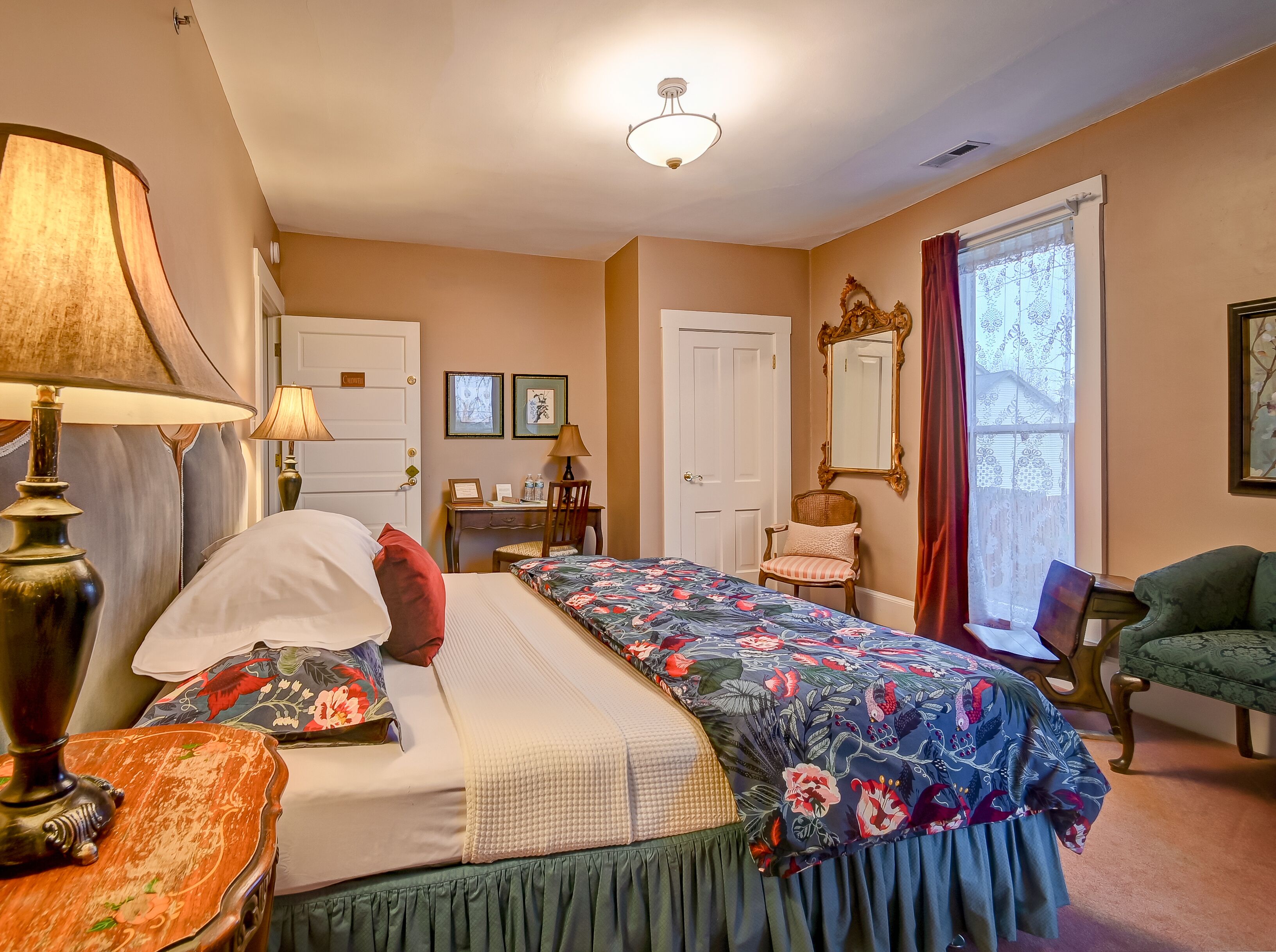 Une chambre bien éclairée, avec un lit, des tables de chevet, une commode, une chaise et une fenêtre avec des rideaux.