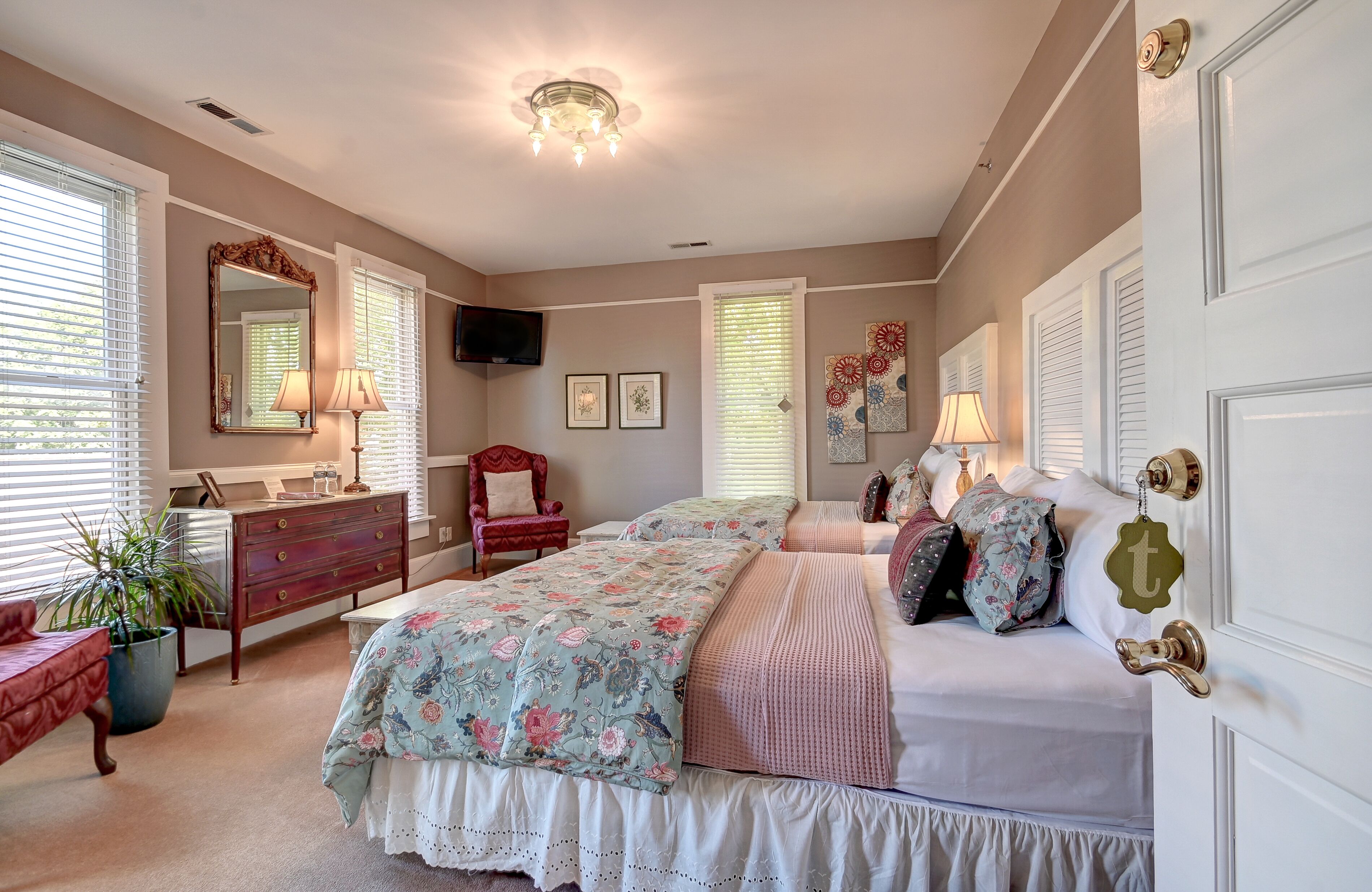 A bedroom with a bed, dresser, chair, and a television on the wall.