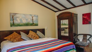 Ein Schlafzimmer mit einem großen Bett, einem hölzernen Kopfteil, einer farbenfrohen Decke und einem Sessel mit Kissen im Zebra-Muster.