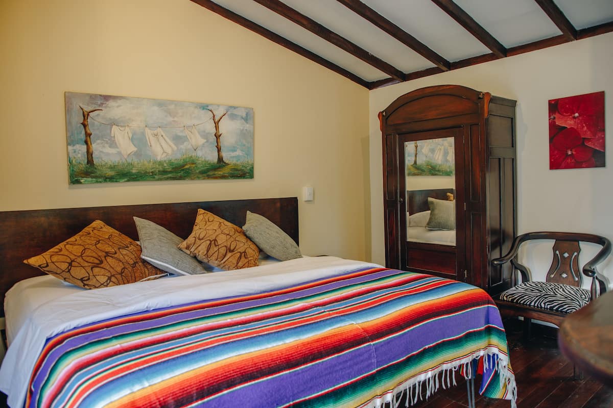 Ein Schlafzimmer mit einem großen Bett, einem hölzernen Kopfteil, einer farbenfrohen Decke und einem Sessel mit Kissen im Zebra-Muster.