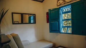 Ein Zimmer mit einer weißen Couch, einem Spiegel, einem Fenster mit blauen Lamellen und einem gefliesten Tisch.