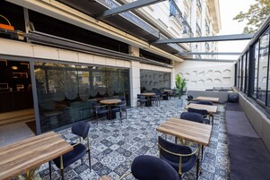 Un café al aire libre con mesas y sillas, un suelo estampado y vistas a un edificio con balcones.