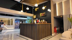 A hotel reception area with a modern design, including a reception desk, pendant lighting, and a large poster advertising the hotel.