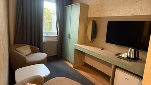 A modern hotel room with a sofa, a small table, a television, a cabinet, and a mini-fridge.