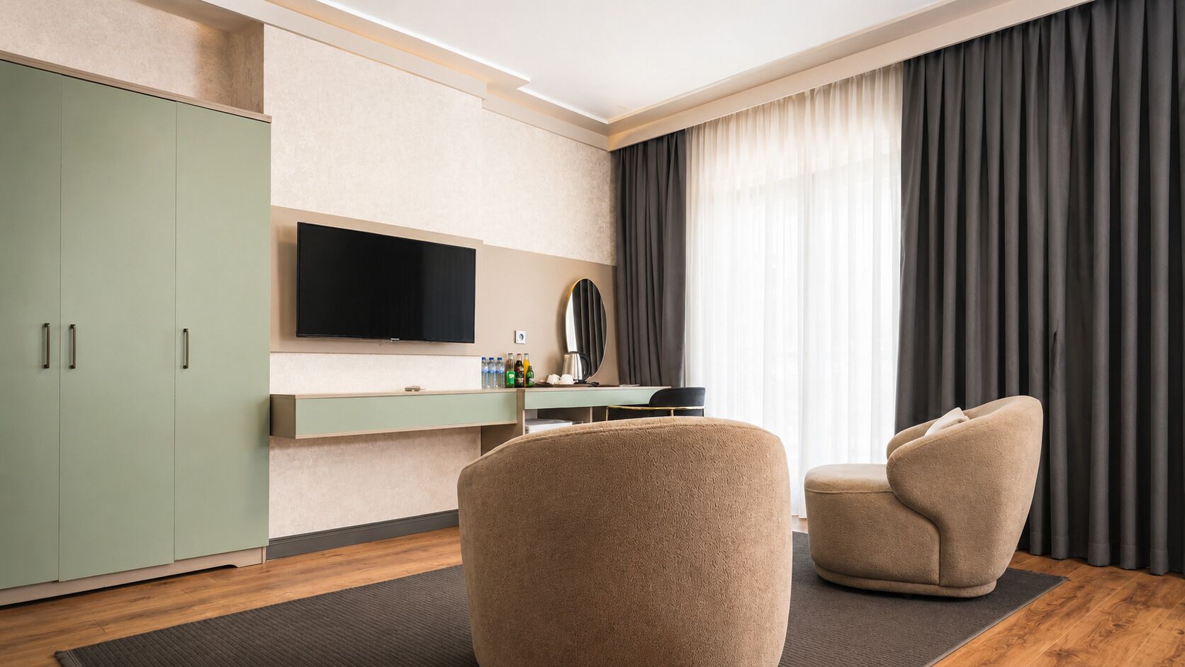 A modern hotel room with a flat-screen TV, a minibar, a sofa, and a large window with curtains.
