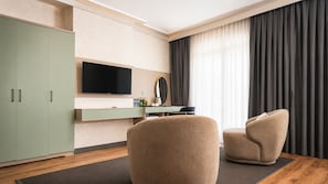 A modern hotel room with a flat-screen TV, a minibar, a sofa, and a large window with curtains.