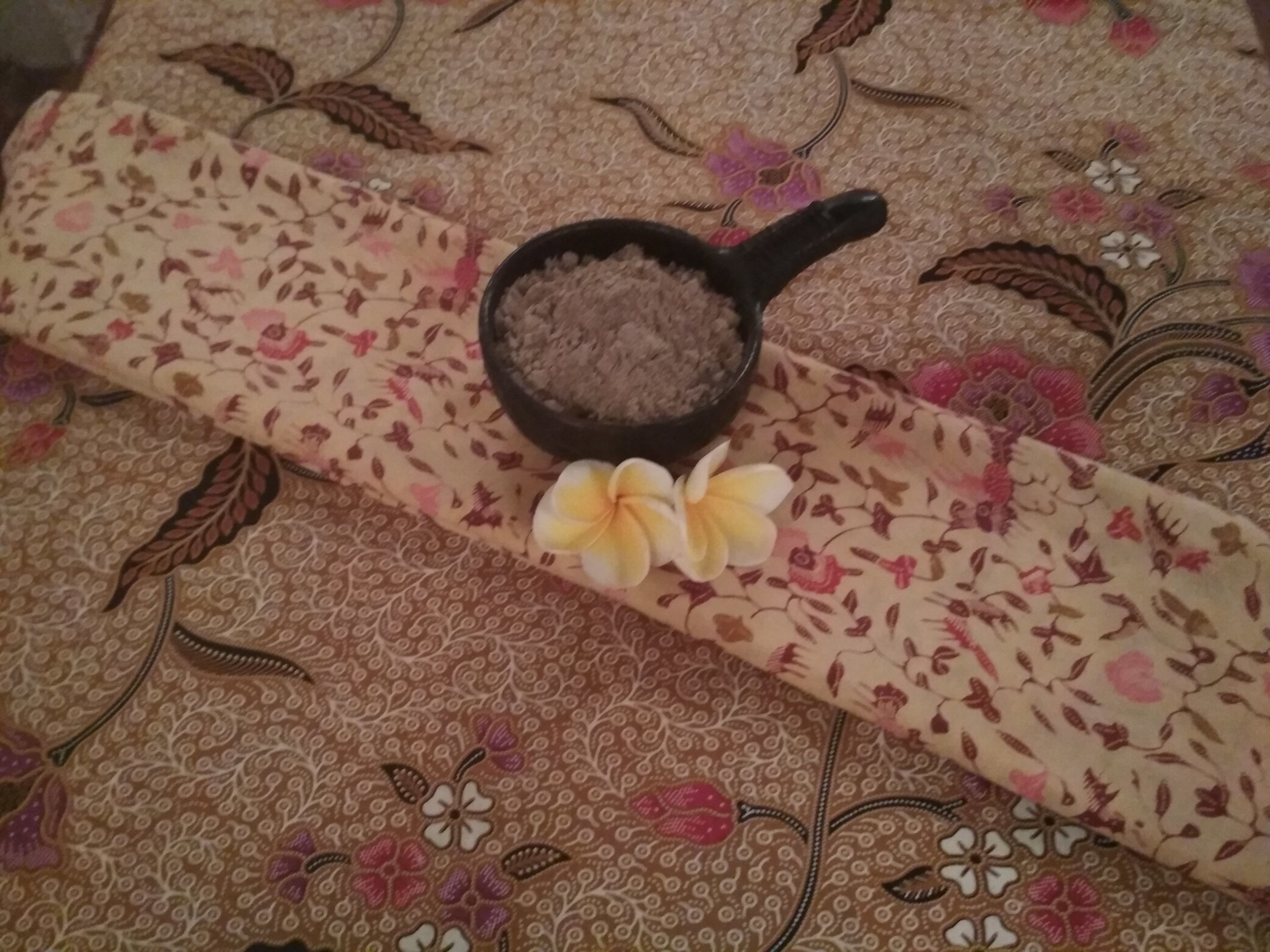 A patterned fabric with a floral design and a small black bowl with a powdery substance on it.