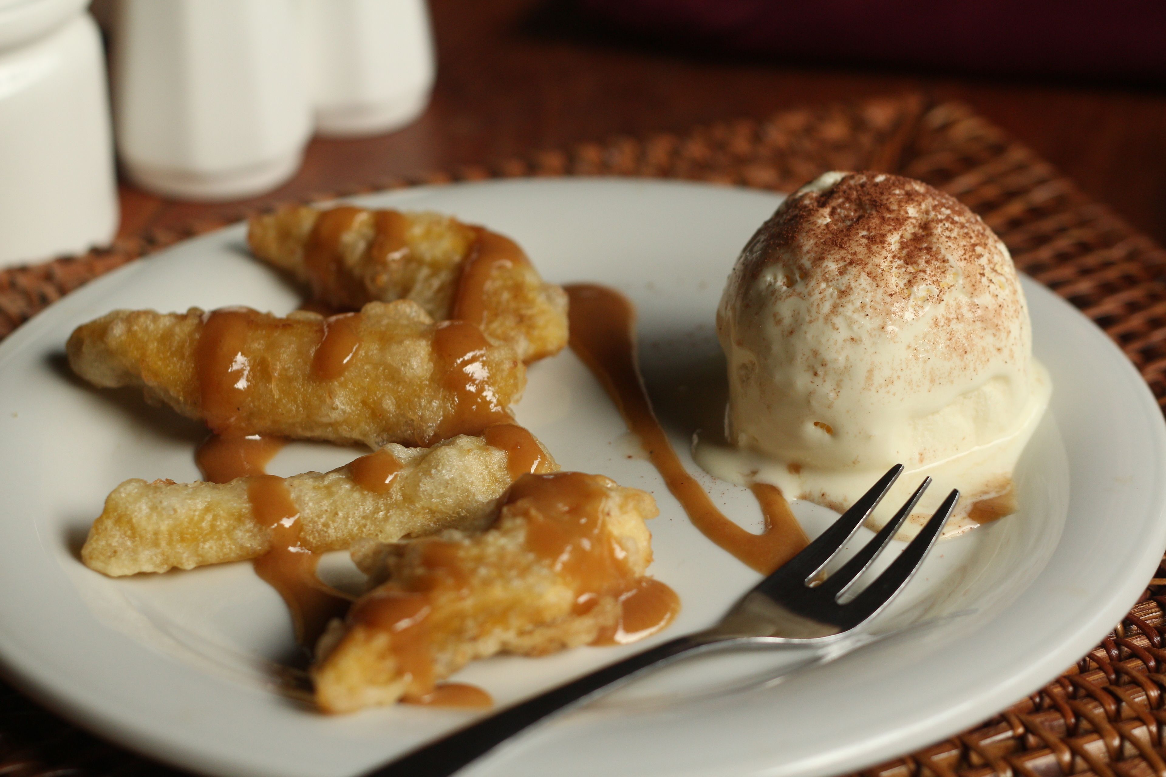 A plate with a dessert consisting of a scoop of ice cream and caramel sauce, accompanied by a fork.