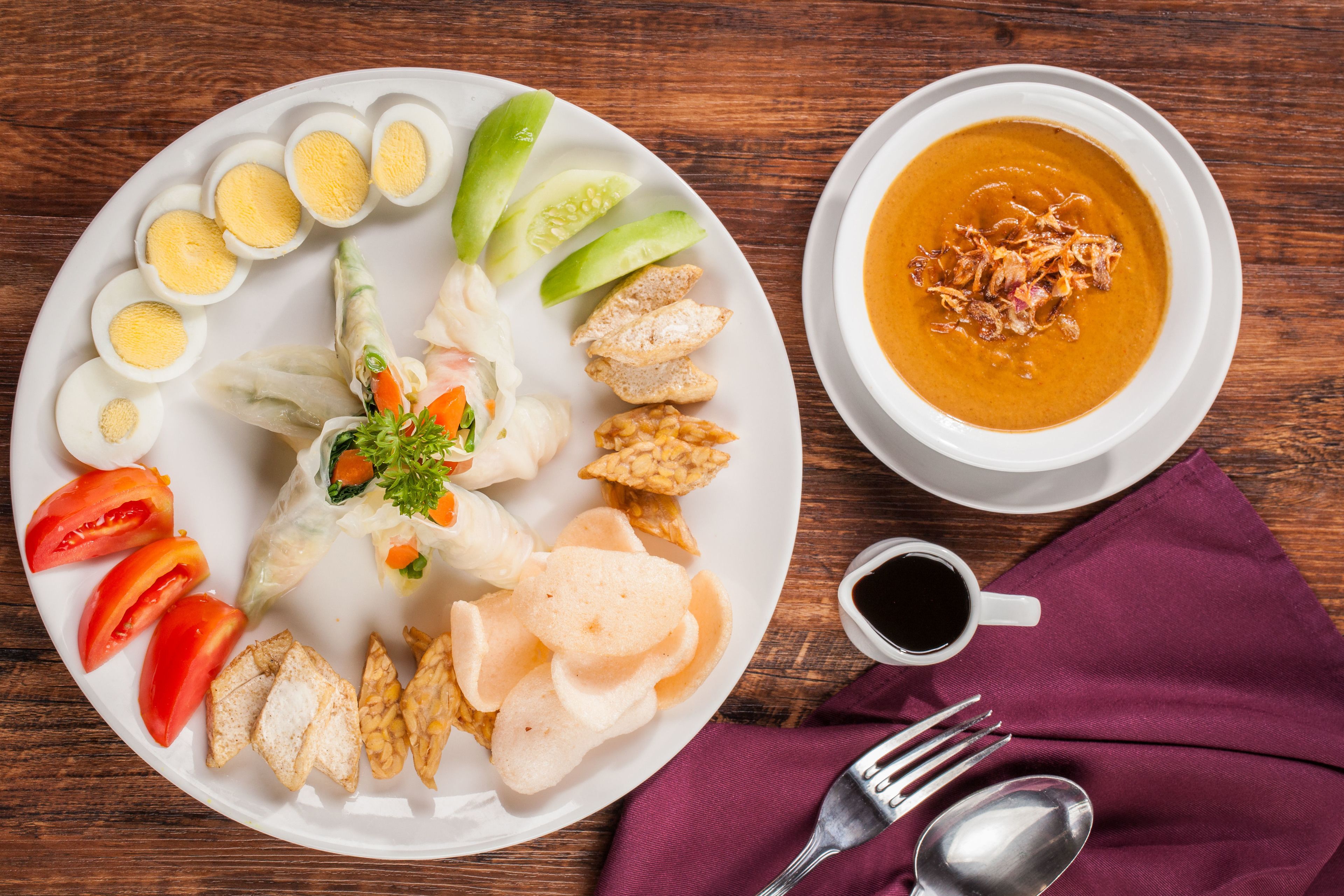 A plate of food including boiled eggs, cucumber slices, and a bowl of soup.