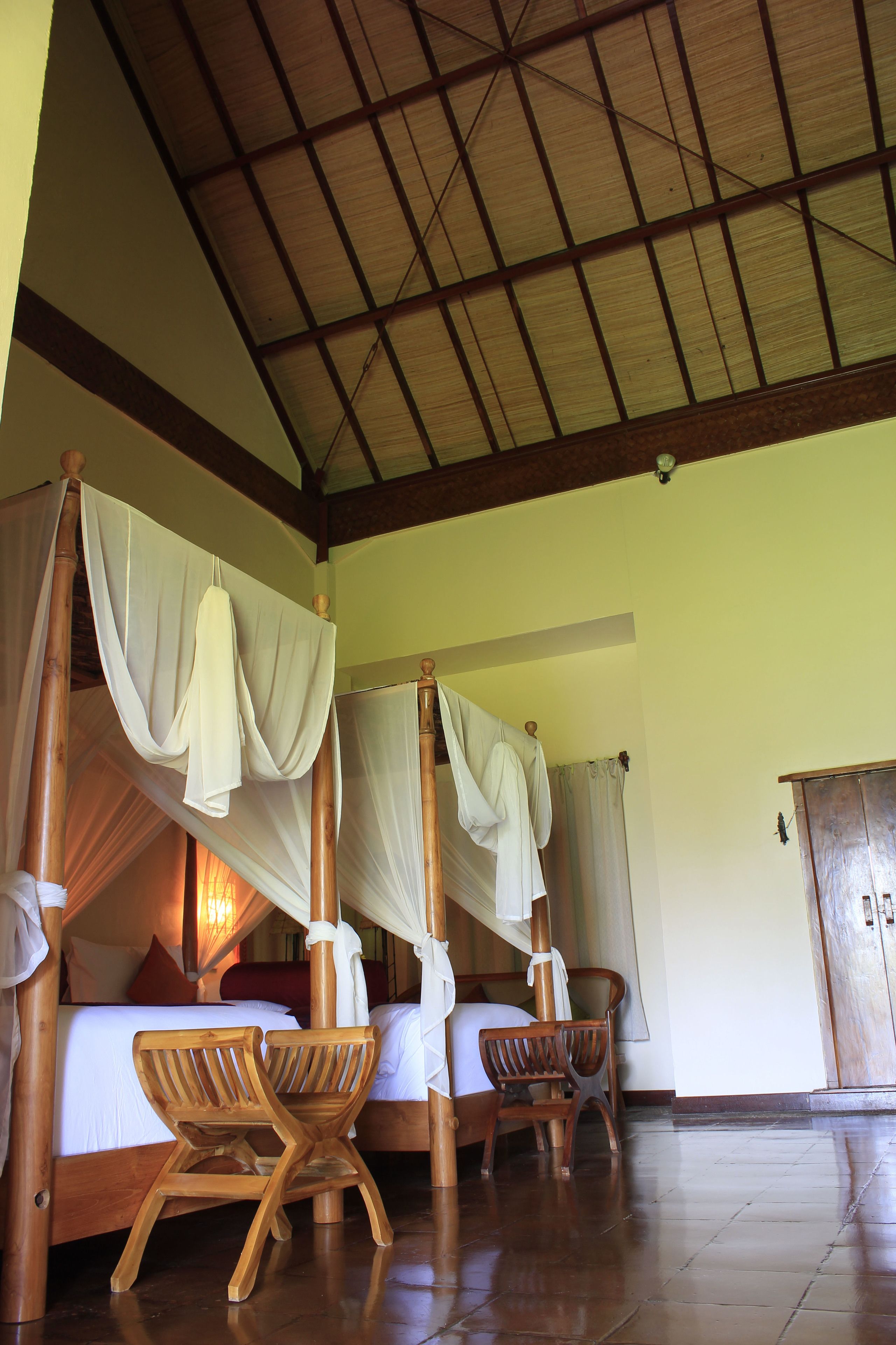 Quarto com cama de dossel, cadeiras de madeira e chão de azulejos.