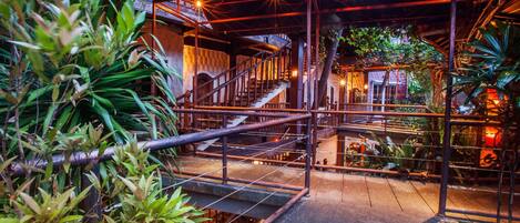 A covered outdoor area with a metal staircase, surrounded by lush greenery and warm lighting.