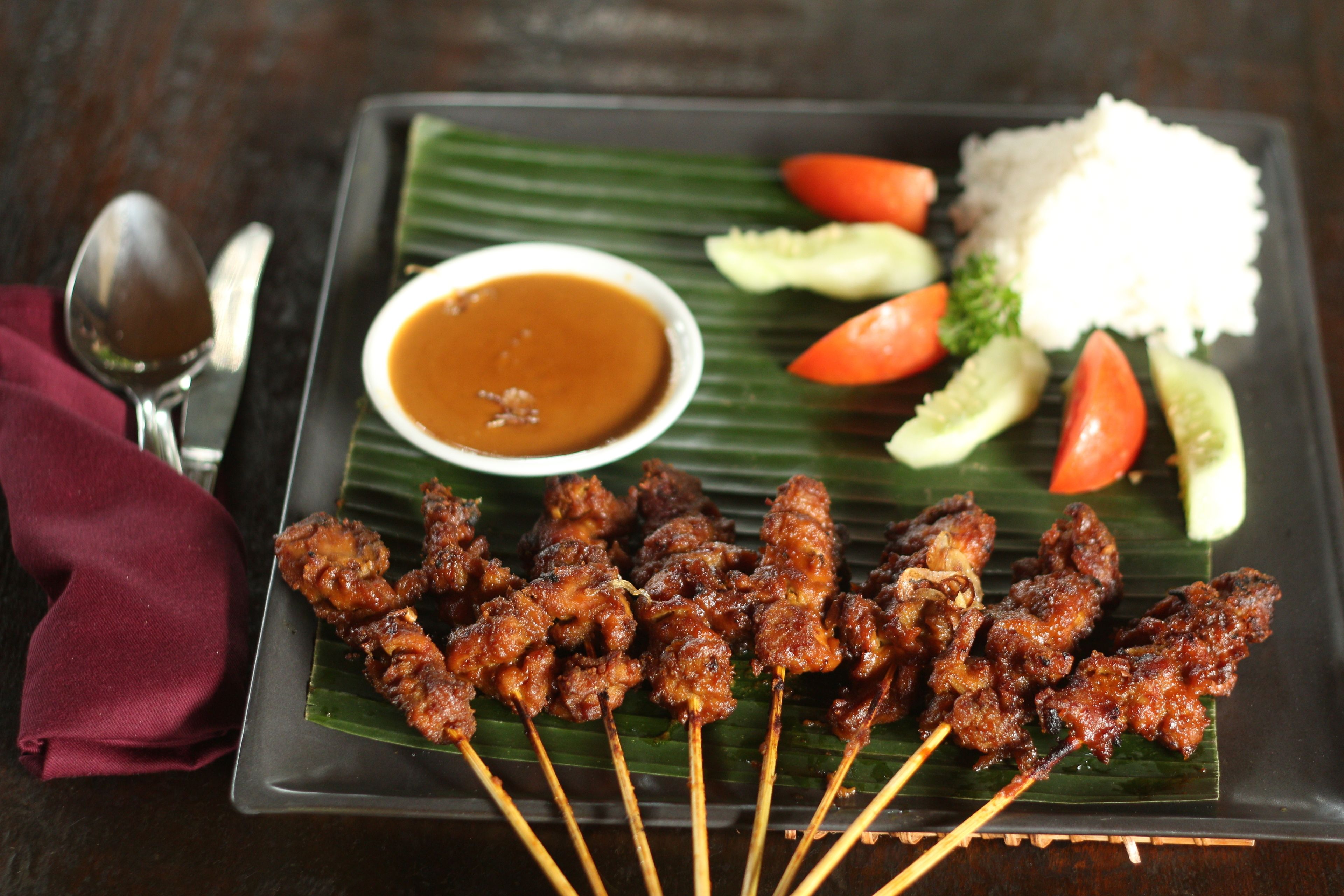 A plate of skewered meat, rice, and vegetables with a side of sauce.