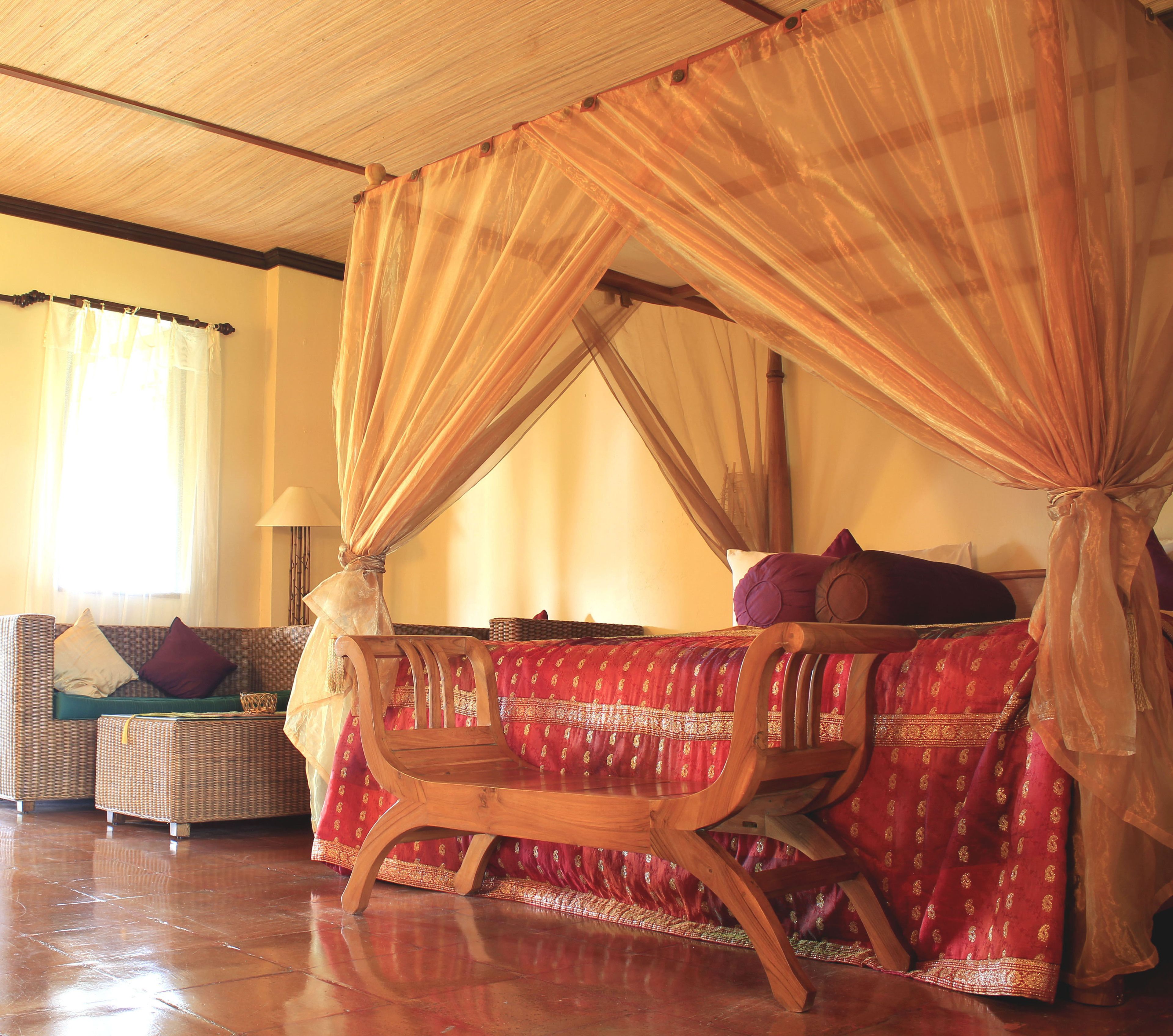 A room with a canopy bed, a sofa, and a wooden chair.