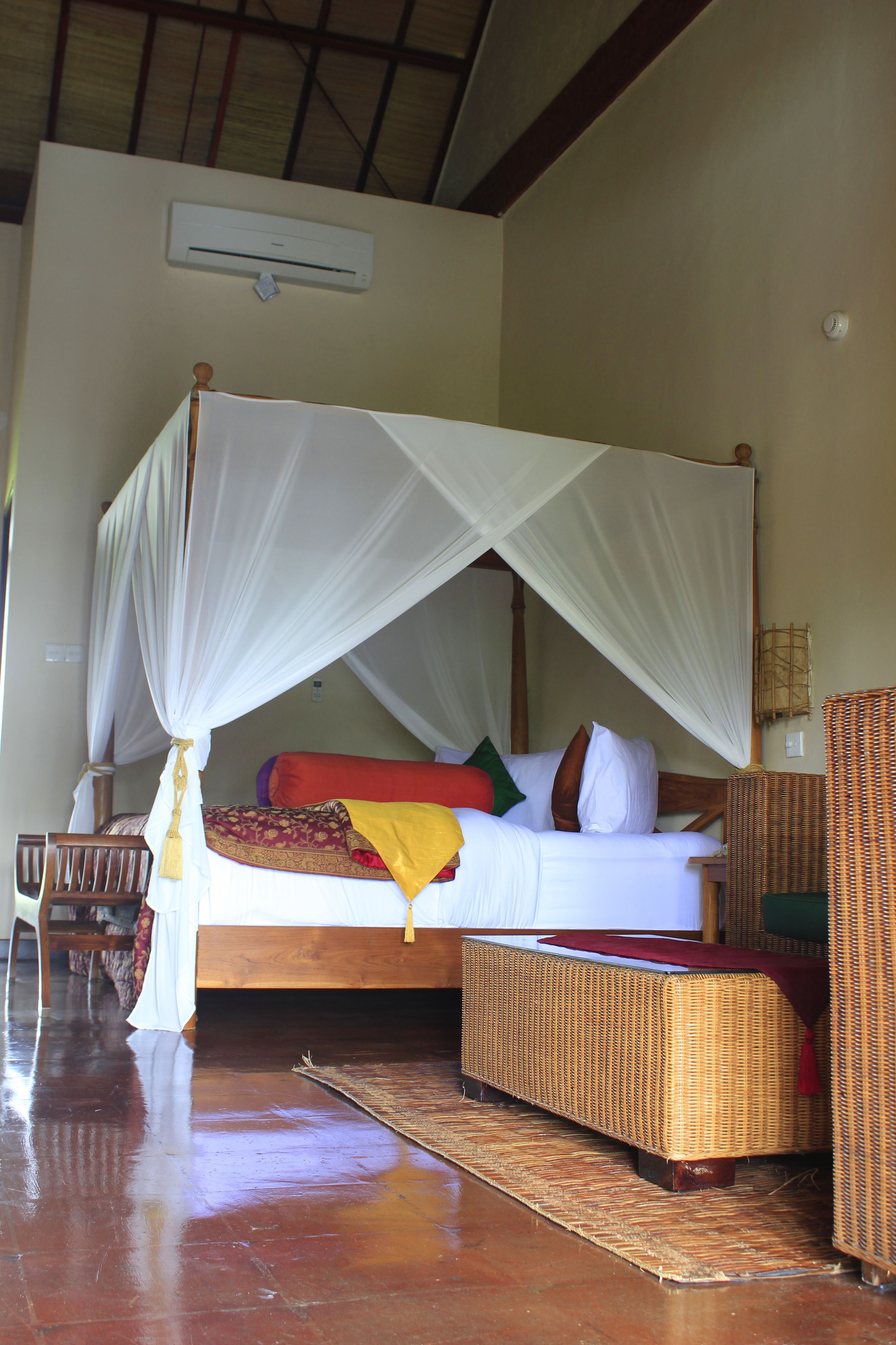 A four-poster bed with a canopy, a wicker chair, and a small table.