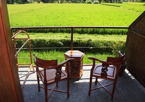 A balcony with two wooden chairs and a small table, overlooking a lush green field.