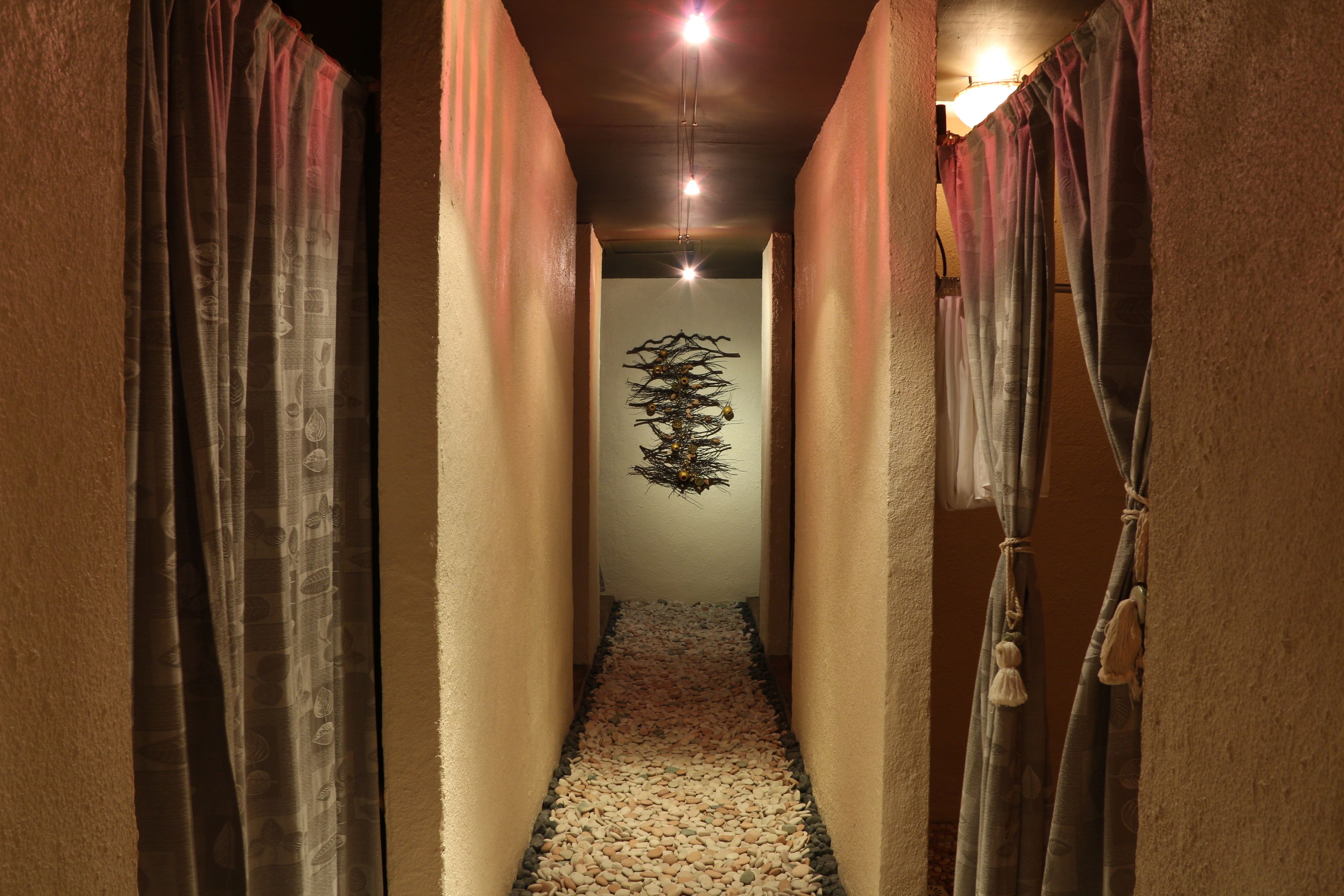 A narrow hallway with patterned curtains on either side, a pebbled floor, and a hanging light fixture in the center.