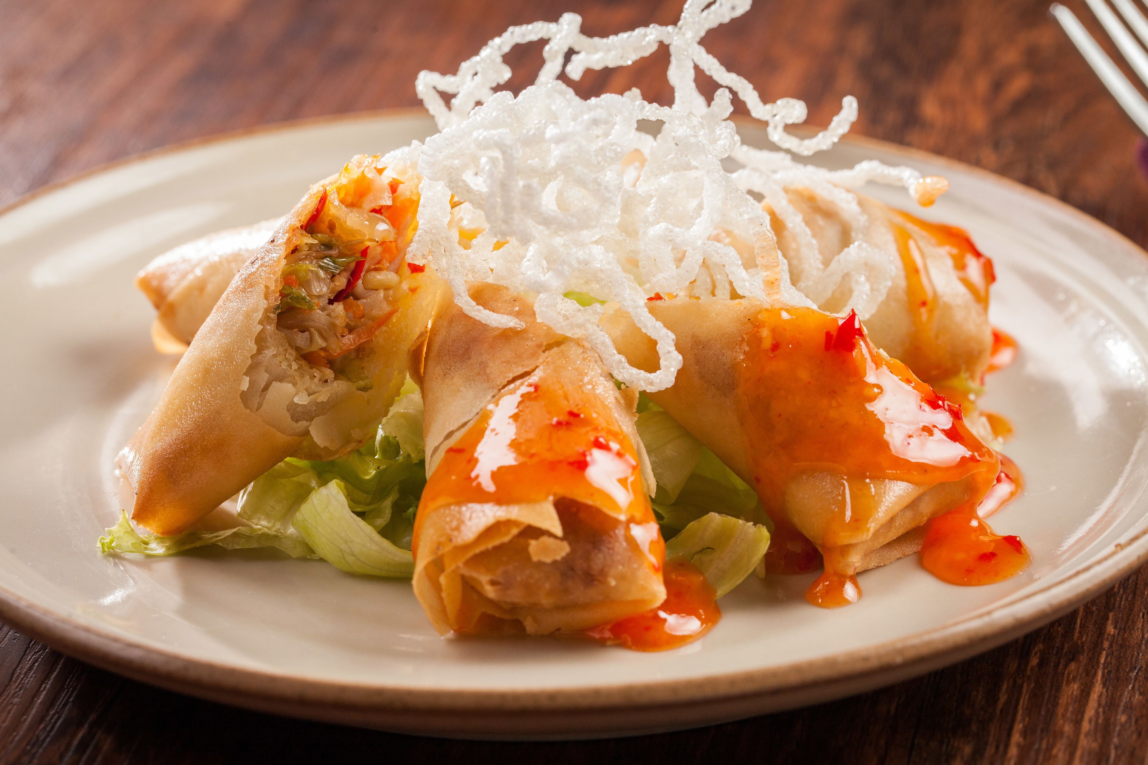 A plate of spring rolls with a sauce and shredded topping.