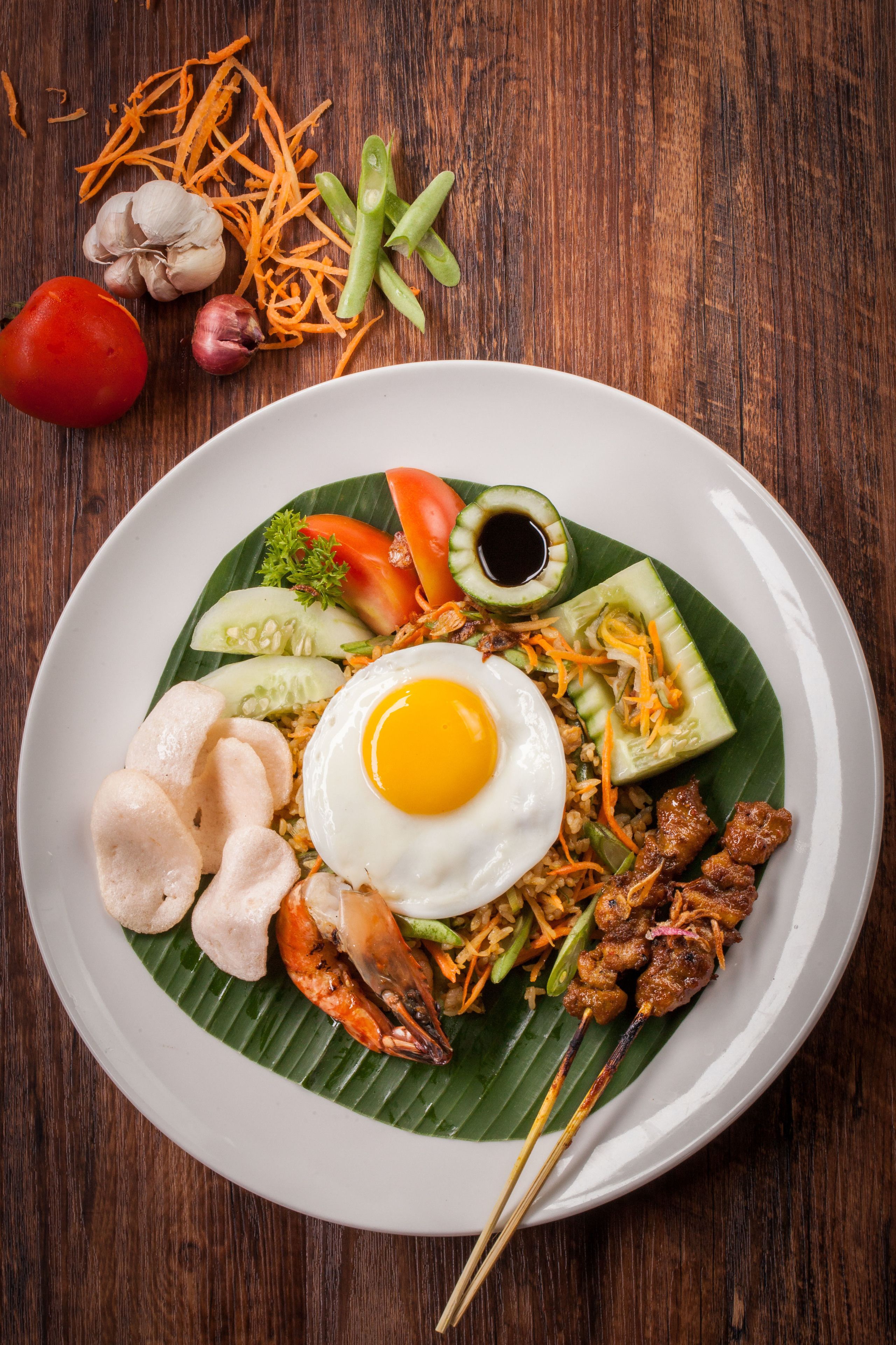 A plate of food with a fried egg, vegetables, and meat on a banana leaf.