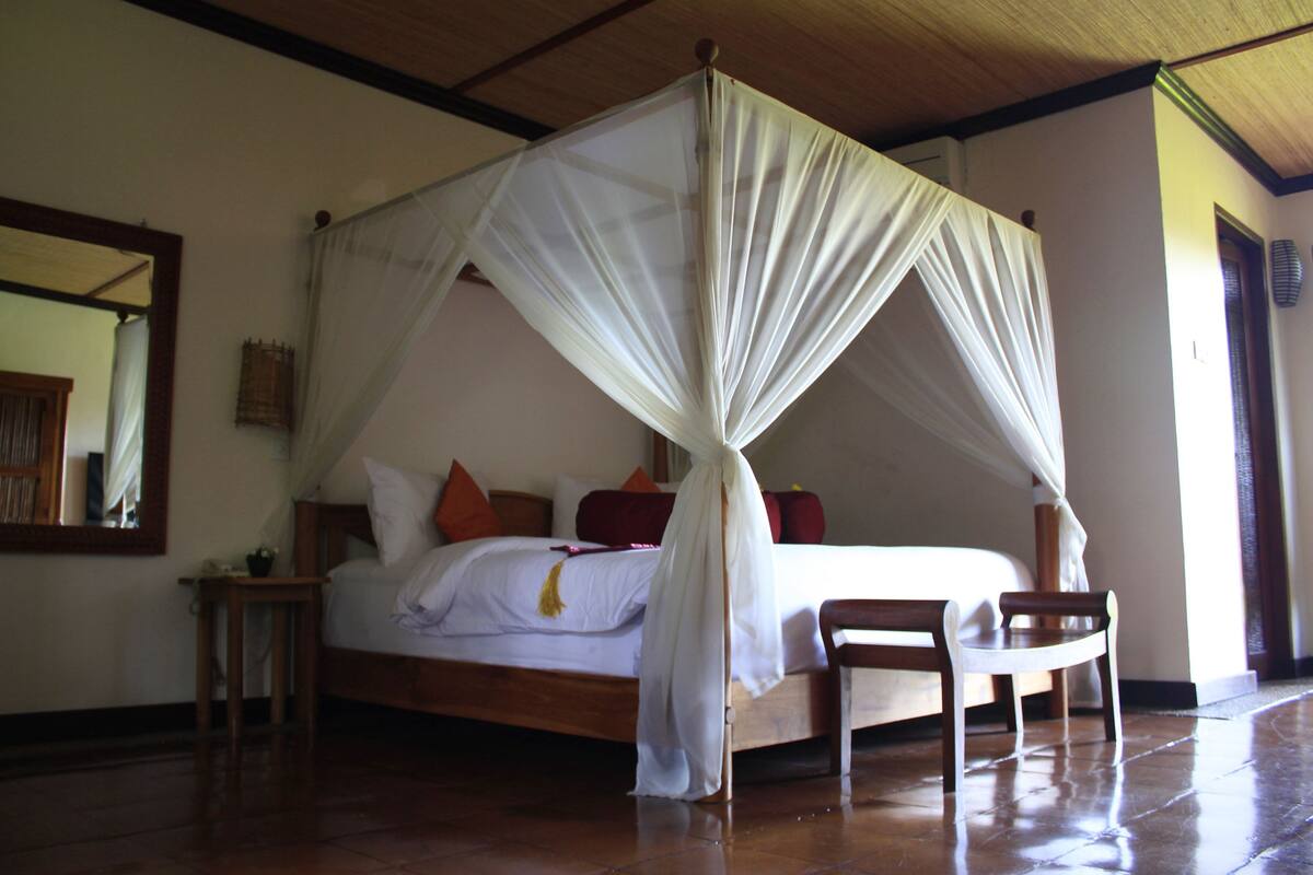 A bedroom with a four-poster bed, a wooden chair, and a nightstand.