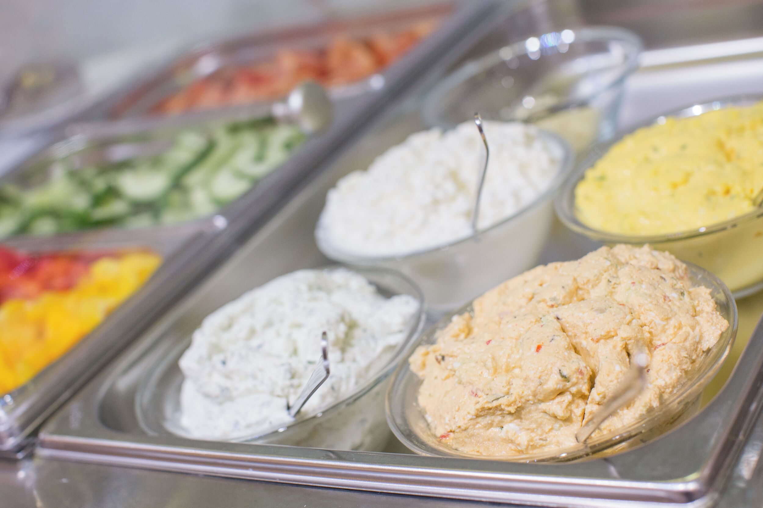 Een buffet met diverse gerechten, waaronder salades, dips en een geel gerecht.