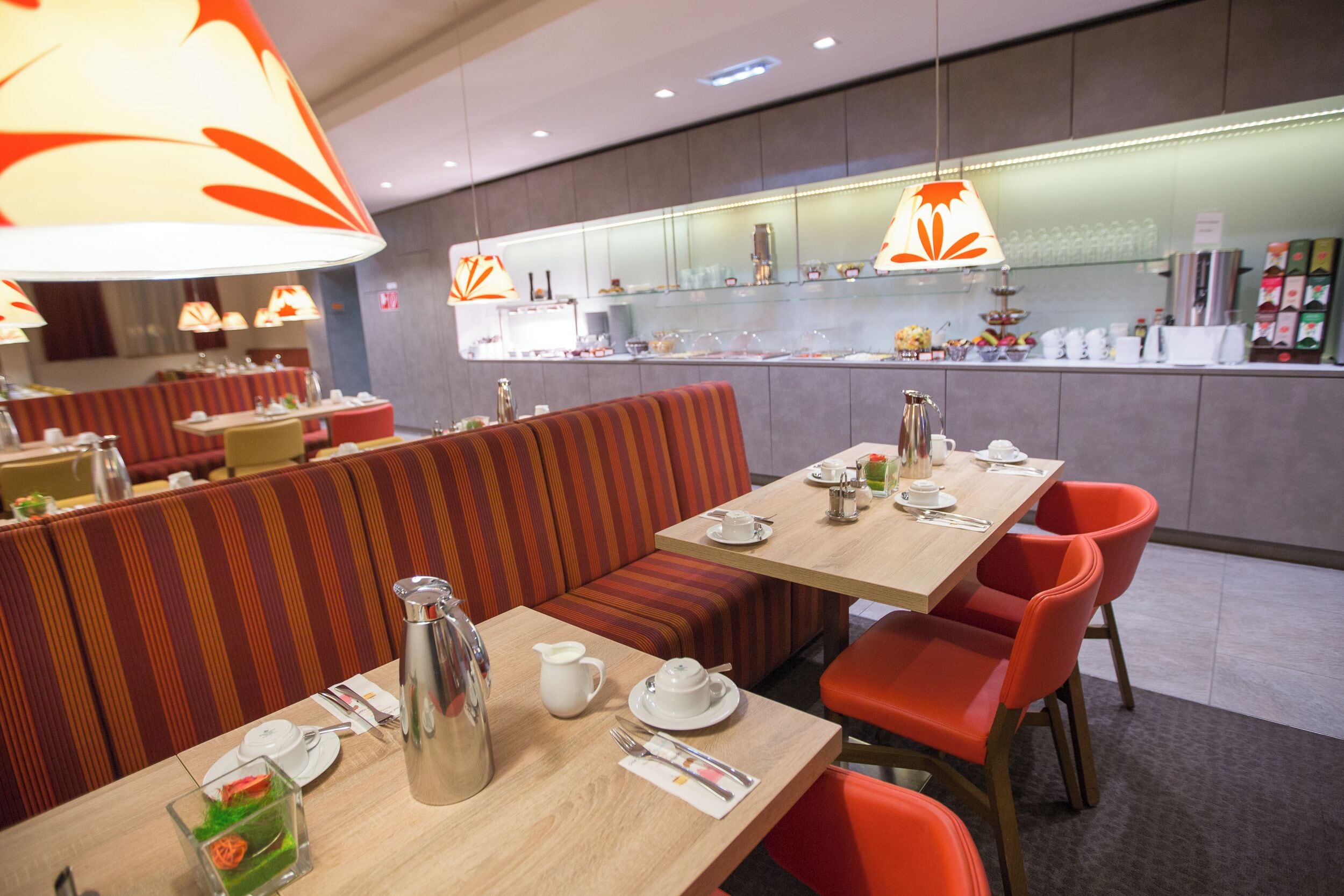 Un restaurante moderno con cabinas a rayas y sillas rojas, un área de bar con mostrador e iluminación colgante.