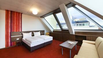 Ein modernes Hotelzimmer mit Bett, einer Couch, einem kleinen Tisch und großen Fenstern mit Blick auf die Stadt.