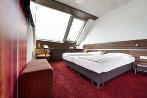 Quarto de hotel moderno com uma cama grande, uma mesa, uma cadeira e um tapete vermelho.