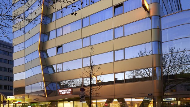 Un hotel moderno con fachada de vidrio, varios pisos y una entrada visible con un letrero.