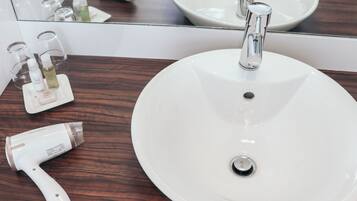 A bathroom with a round white sink, a mirror, and a wooden countertop.