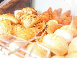 Diversos produtos de panificação, incluindo pão e doces, expostos num recipiente transparente.