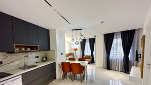 A modern kitchen with dark cabinets, a marble countertop, and a dining area with a table and chairs. - Happy Apart (Kusadasi)