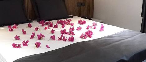 Quarto de hotel com uma cama grande, duas almofadas pretas, um painel de cabeceira de madeira e uma luminária fixada na parede.