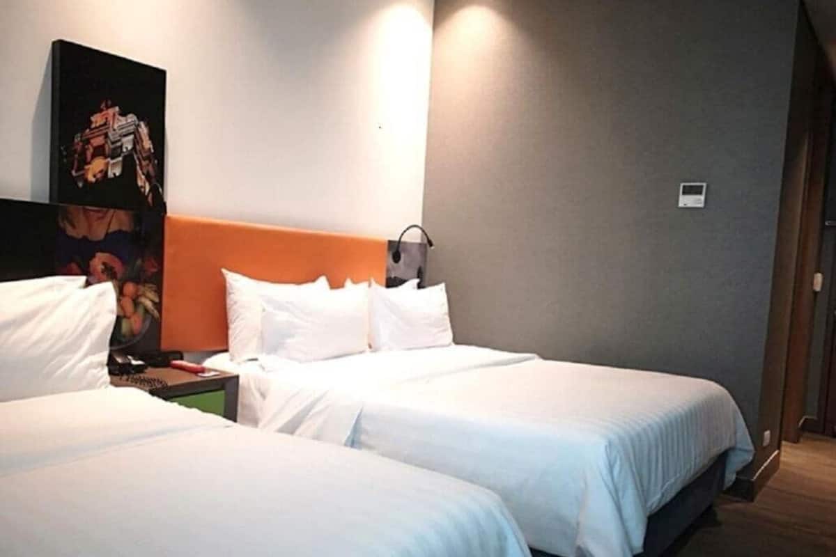 A hotel room with two beds, a nightstand, a wall-mounted light, and a poster on the wall.