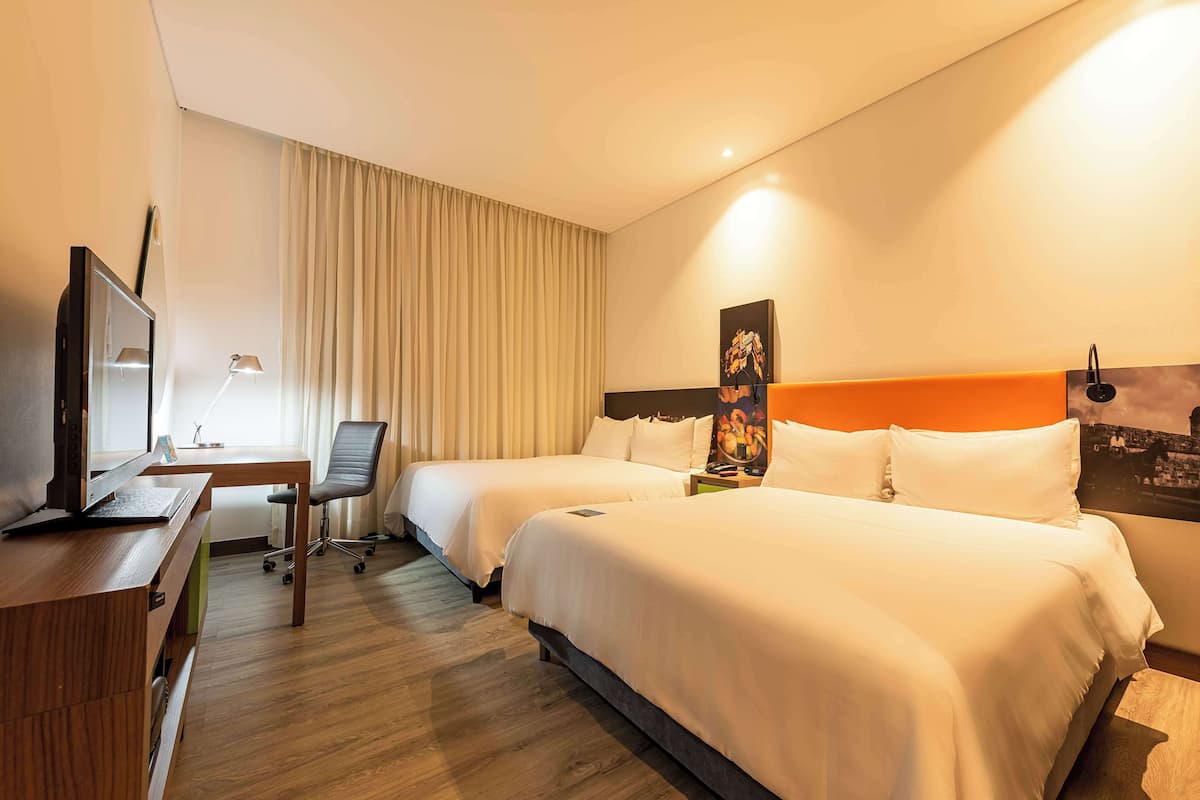 A hotel room with two beds, a desk with a computer, a chair, and a TV.